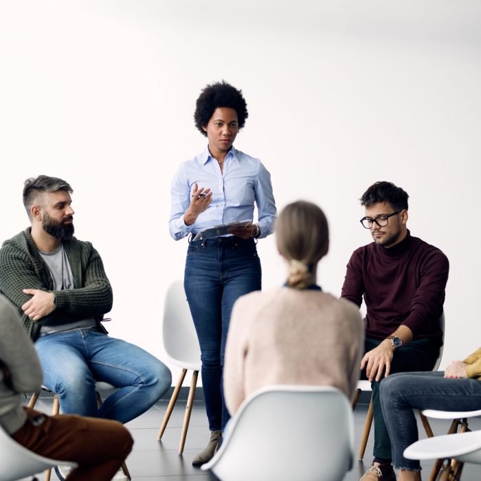 Black female therapist standing while talking to attenders of group therapy at community center.